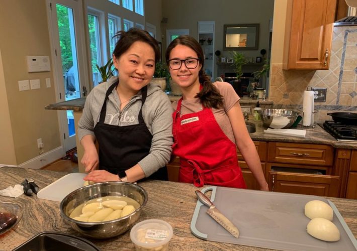 Au pair and host mother cook dinner at kitchen table.