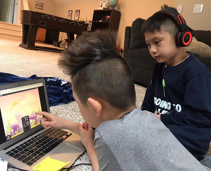 Two young boys sit in front of a computer in a living room playing an educational math game