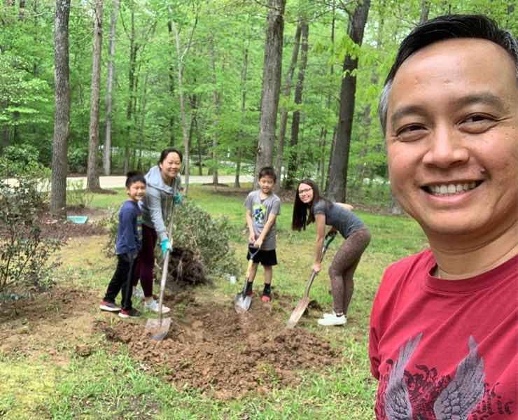 Family of two boys, a host mother, and a host father, with an au pair from Brazil, holding shovels in a yard