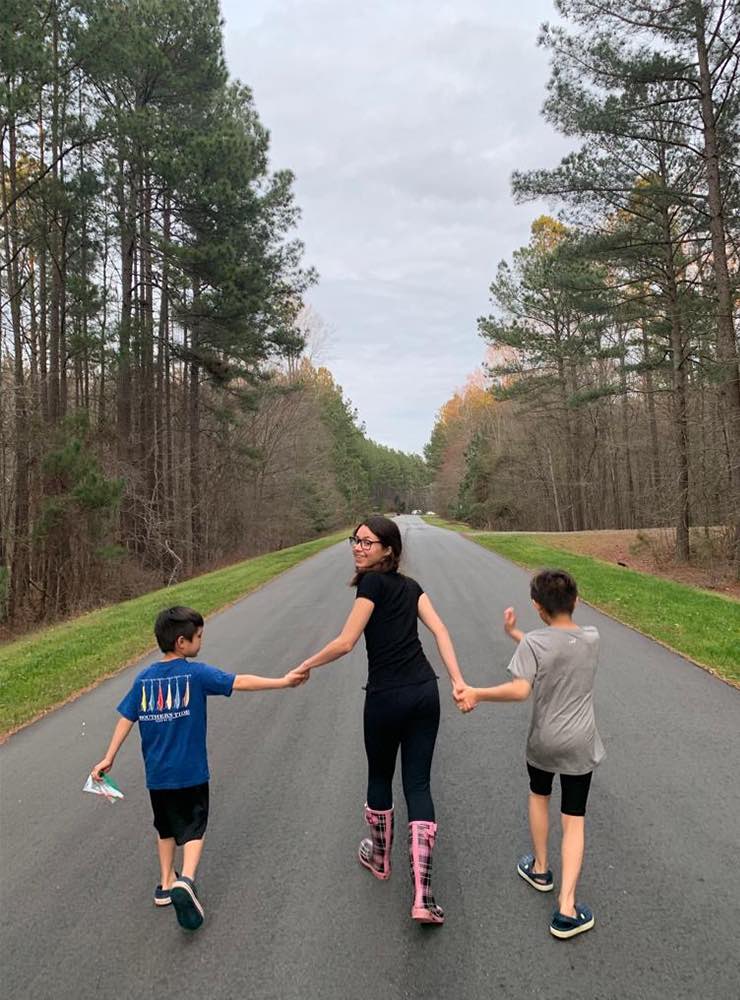 Two boys and an au pair from Brazil walking down a street surrounded by trees