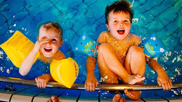 Two kids playing and swimming in a pool with safety floatation devices.