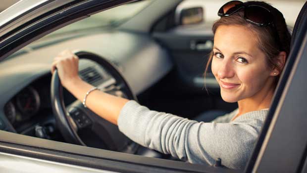 A smiling young woman in a car with a hand on the steering wheel