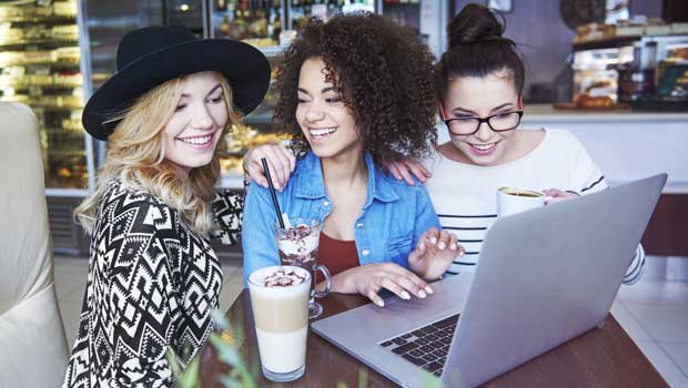 Three young women look at a computer screen in a coffee shop