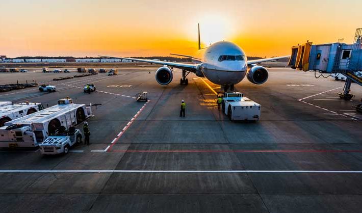 Airplane sits on tarmac as sun sets in the background