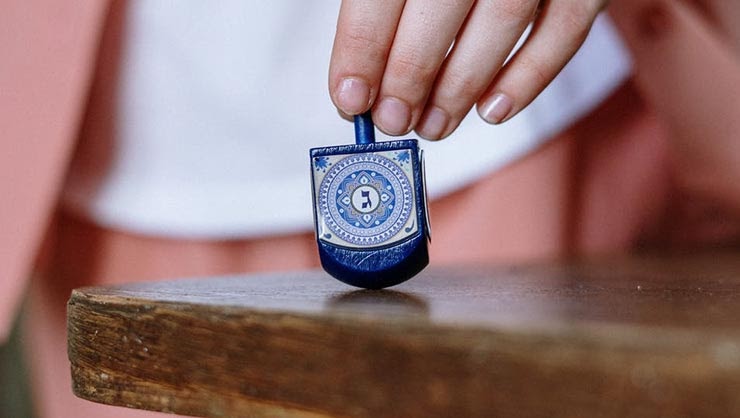 A and grips a blue dreidel on a tabletop.