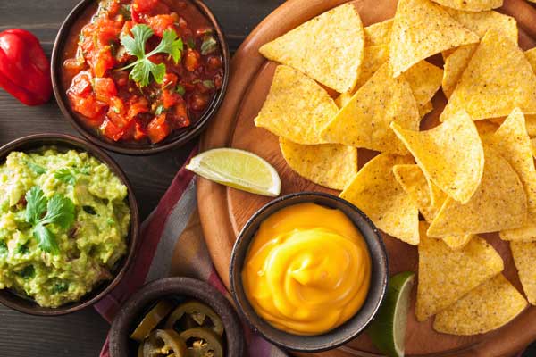 A table with chips, salsa, nacho dip, and guacamole dip.