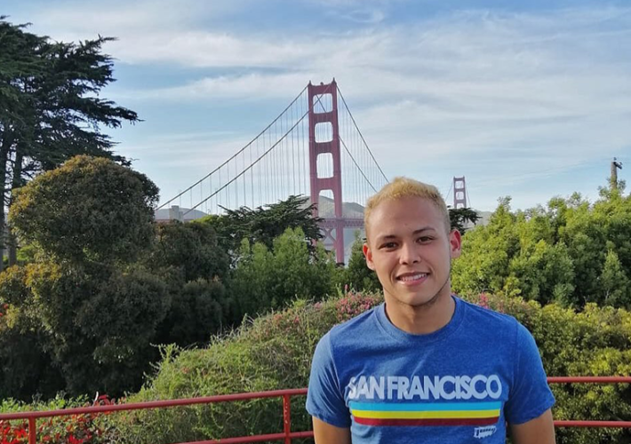 An au pair wearing a San Francisco shirt stands in front of the Golden Gate Bridge.