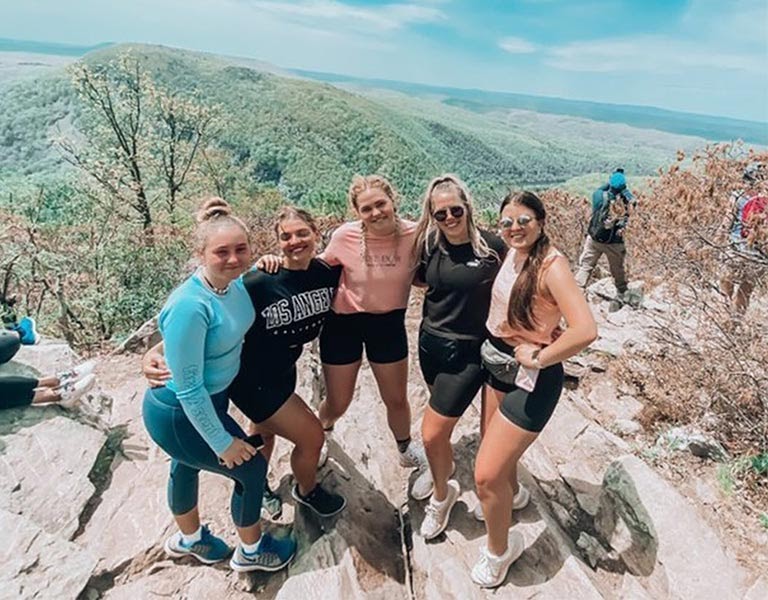 Five woman smile on a mountaintop.