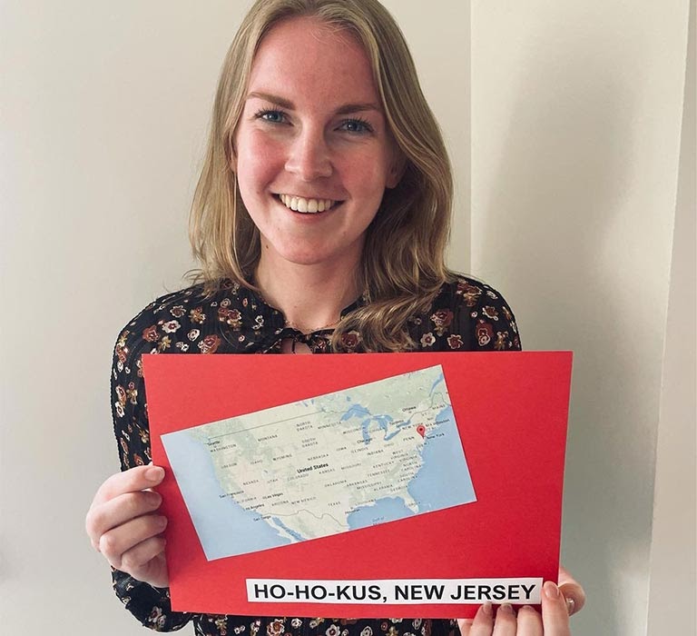 A smiling woman holds a card with a map of New Jersey.