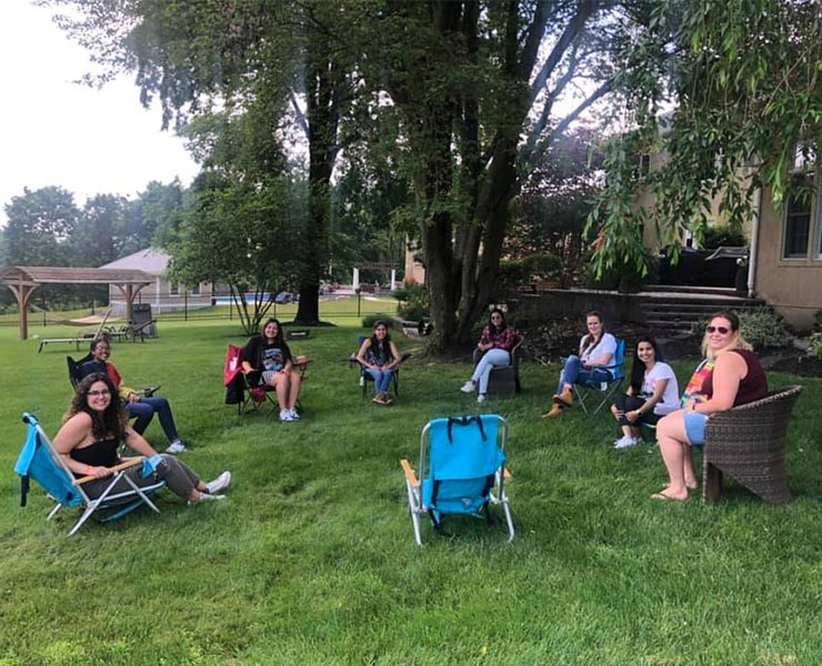 Eight au pairs sit socially-distanced in a circle in a backyard. 