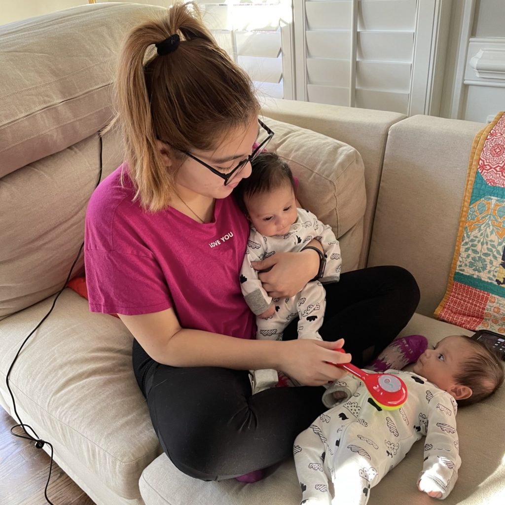An au pair holds one host baby and plays with a second host baby.