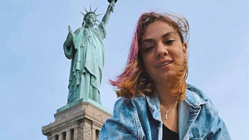 Young woman poses smiling in front of the Statue of Liberty.