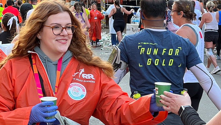A young woman dressed in orange passes a cup of Gatorade to a marathon runner