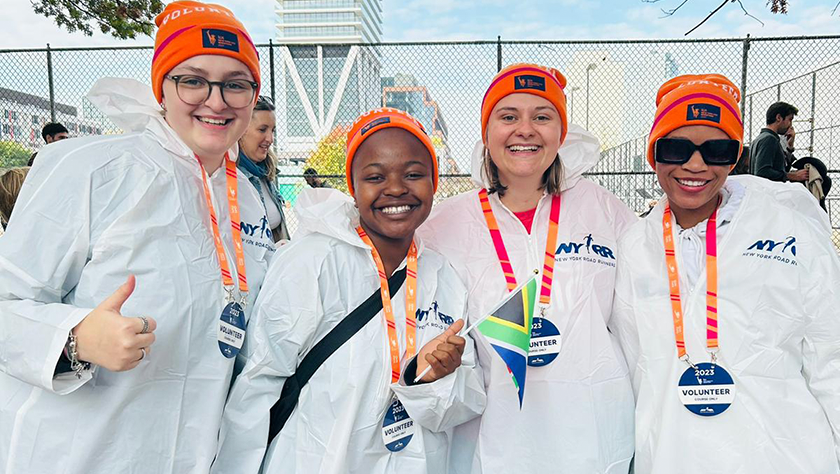 Four young women pose wearing marathon volunteer ponchos and ski caps