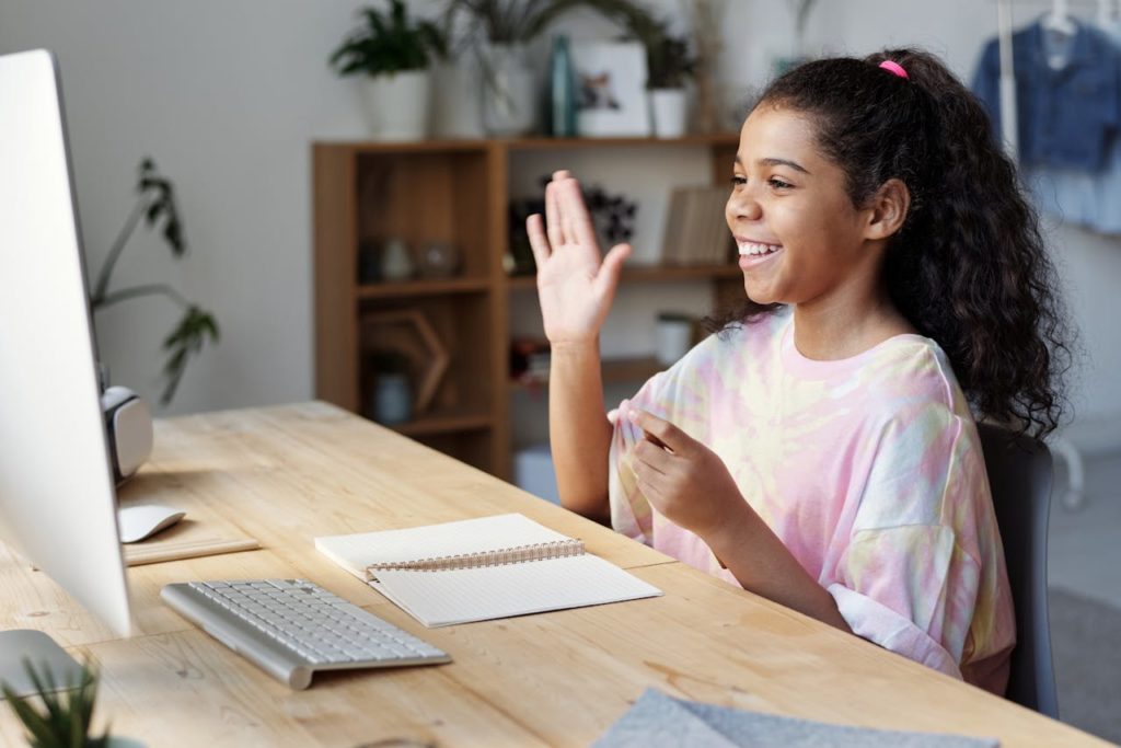 Young girl waving to a computer screen.