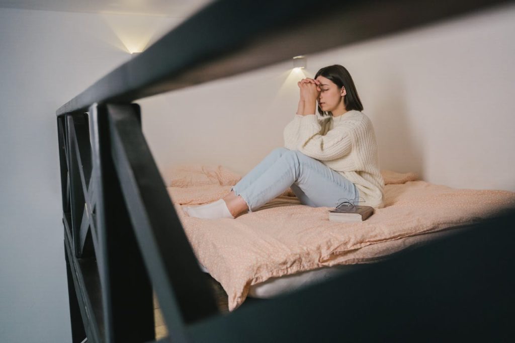 Woman sitting on her bed, deep in thought.