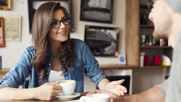 Young woman speaks to man while both drink coffe