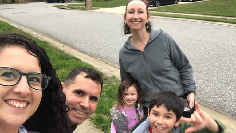 Au pair and host family stand on the sidewalk smiling.