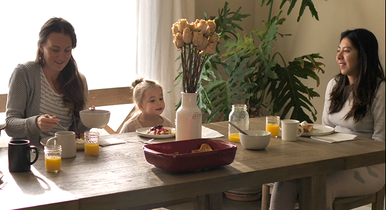 An au pair, a host mom, and a host child sit at a dining table.