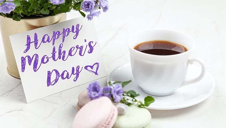 A "Happy Mother's Day" card next to flowers, cookies, and a cup of tea.