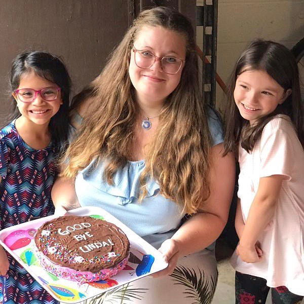 An au pair holds a cake with host kids.